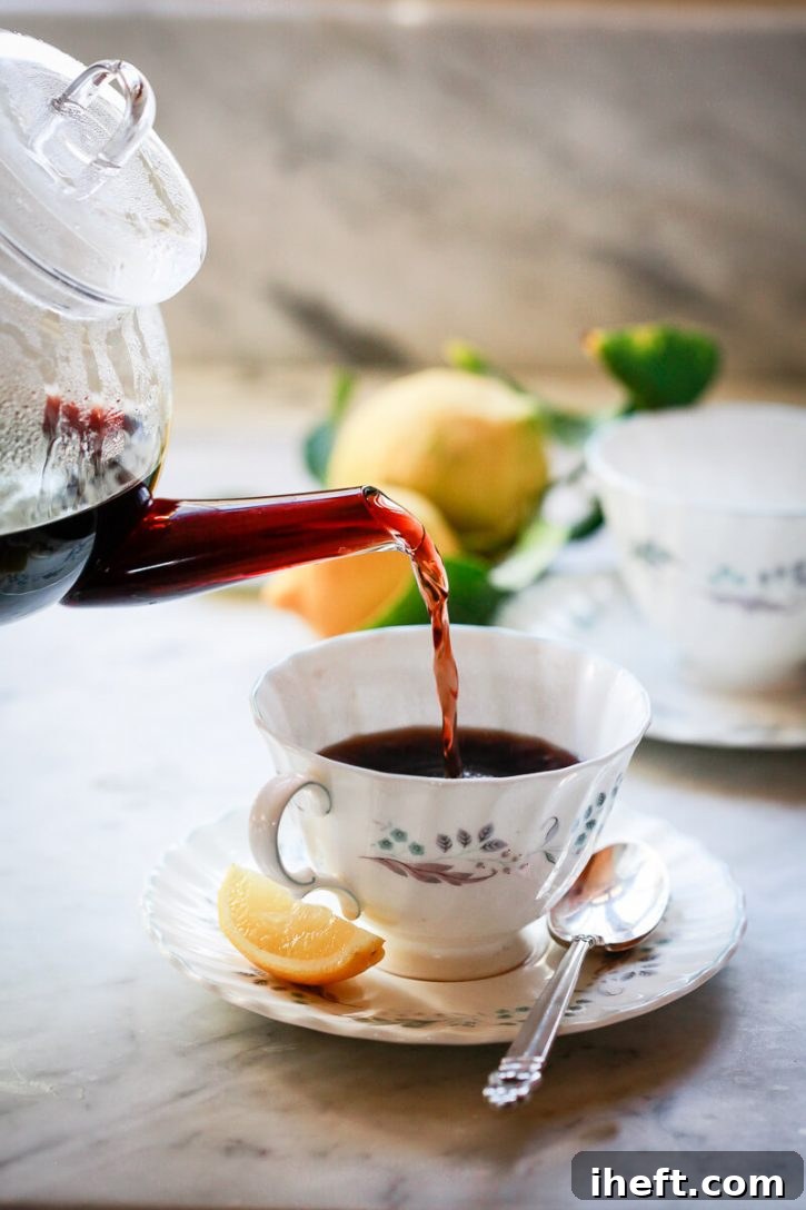 Homemade elderberry tea pours from a teapot into a teacup. This homemade elderberry tea is a natural remedy for cough, cold, and flu. 