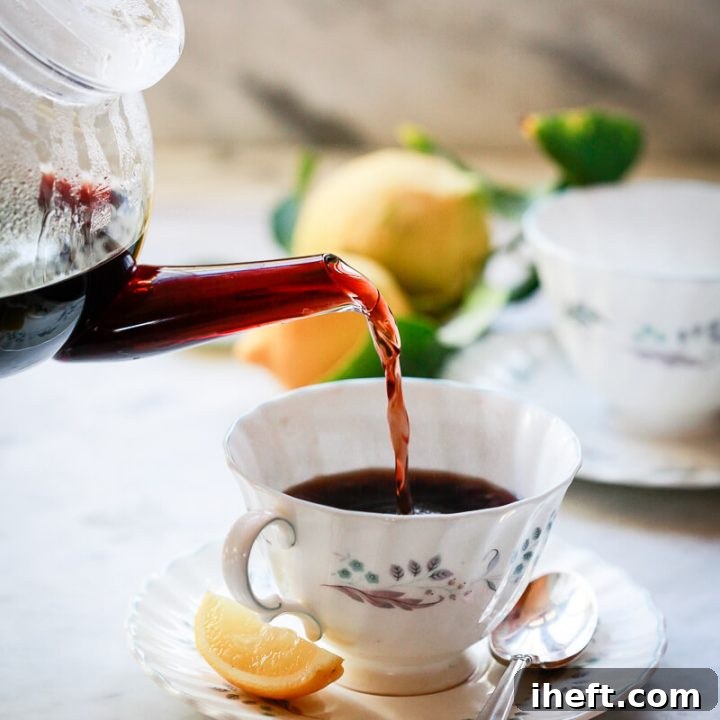 A teapot pours homemade elderberry tea into a teacup.
