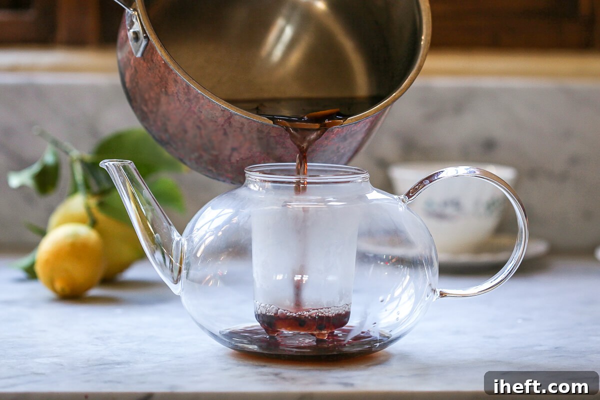 Homemade elderberry tea is strained into a teapot.