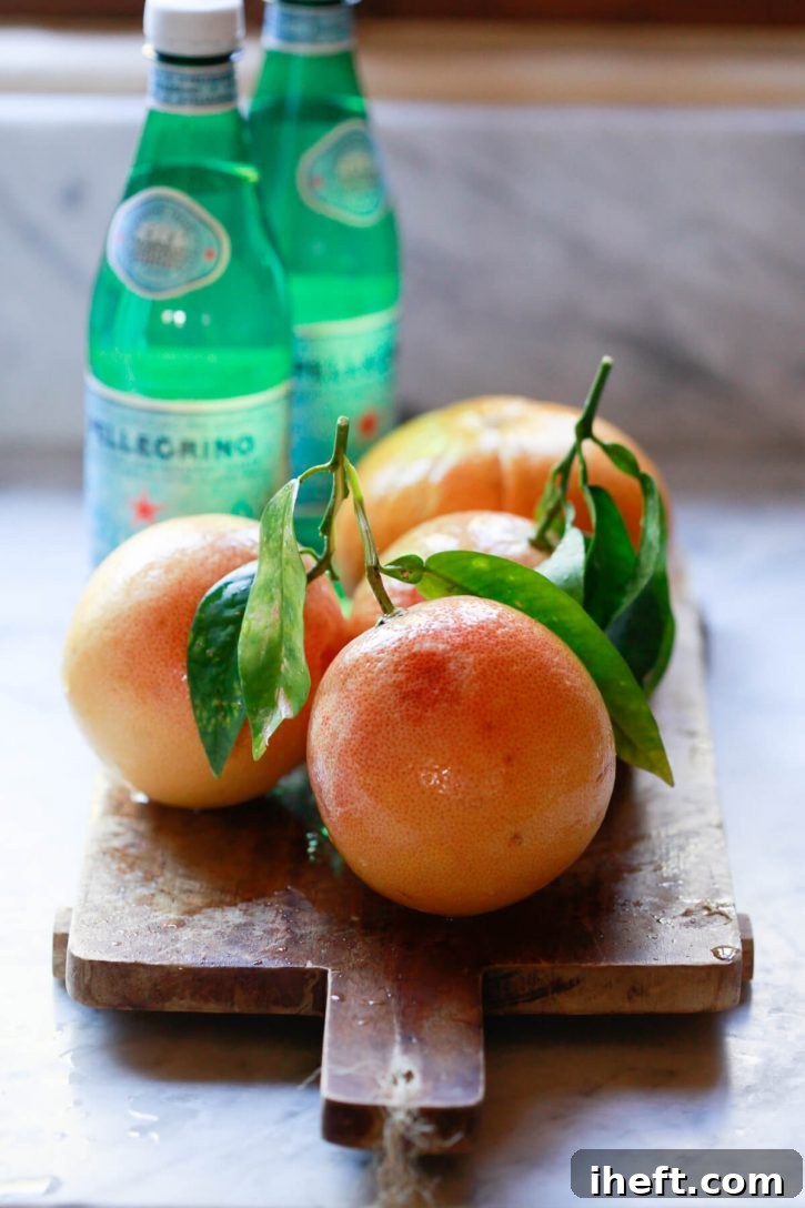 Homegrown grapefruits and bottles of San Pellegrino sparkling water on a marble countertop, showcasing the fresh ingredients needed for homemade grapefruit soda.