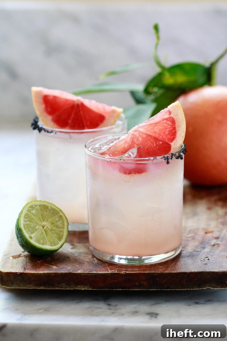 Two Paloma cocktails made with homemade grapefruit soda and tequila, garnished with fresh grapefruit slices, served in a white kitchen setting.