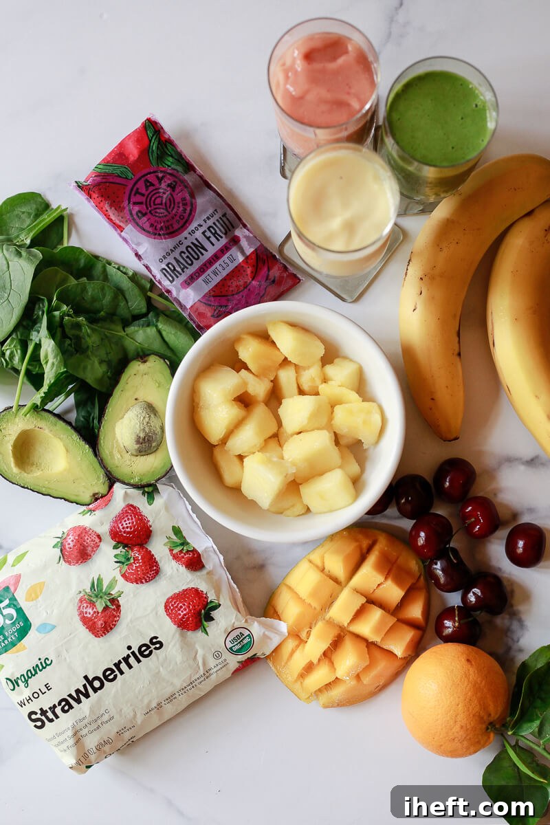 Ingredients for making healthy smoothie recipes on a marble countertop include frozen fruit, avocados, spinach, Dragon fruit packs, bananas, oranges, cherries and mango. 