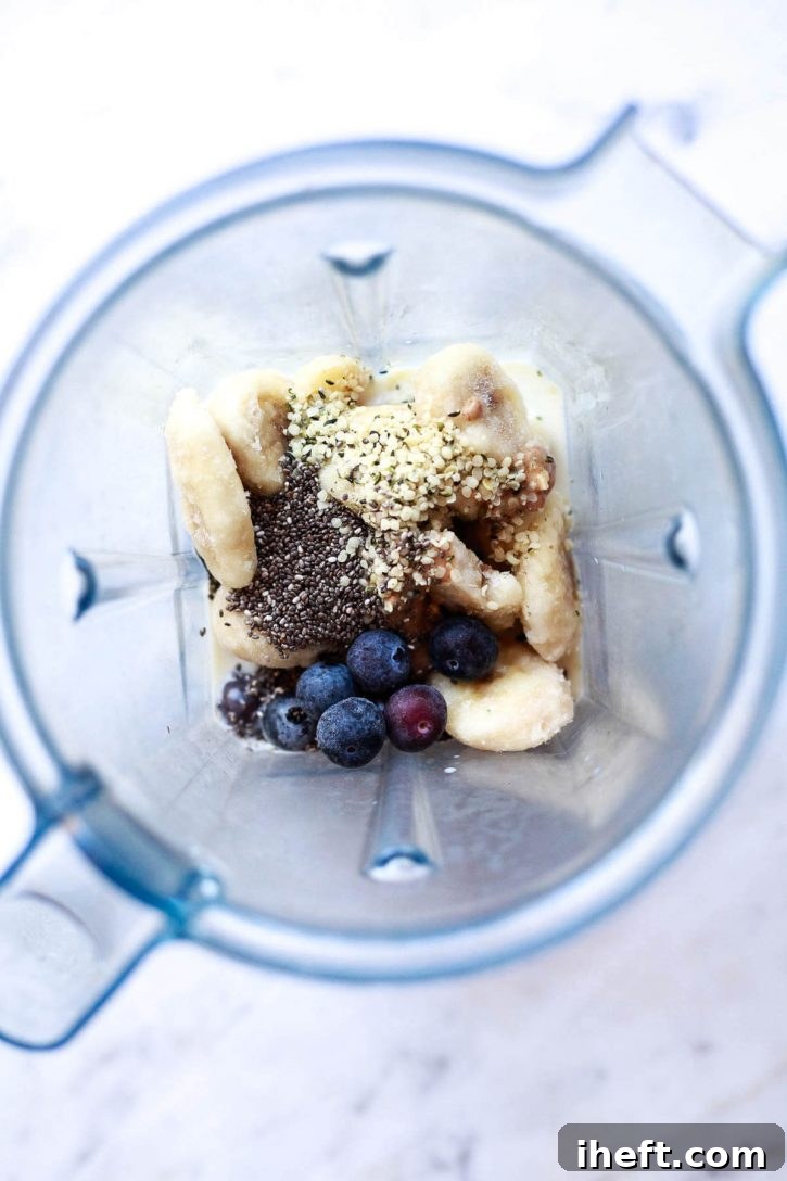 All of the ingredients for a healthy blueberry, chia, and hemp smoothie are seen in a blender. 