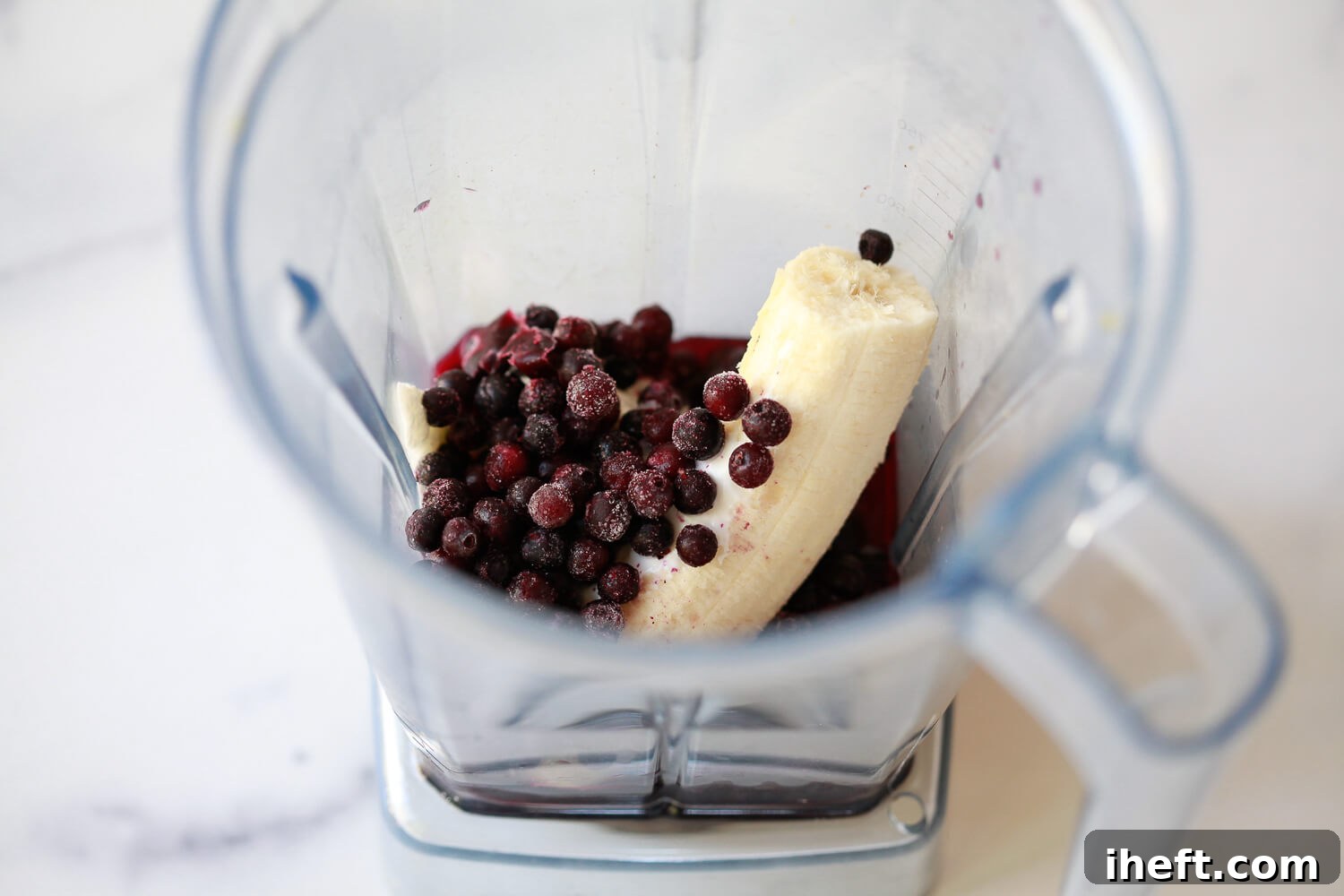 Banana, yogurt, and frozen blueberries in a blender to make a healthy smoothie.