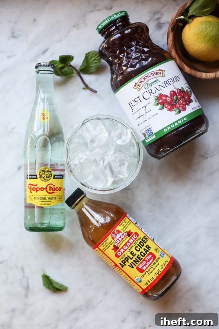 The simple ingredients for a cranberry detox water drink laid out on a kitchen countertop: unsweetened cranberry juice, sparkling water, ice, and organic apple cider vinegar.