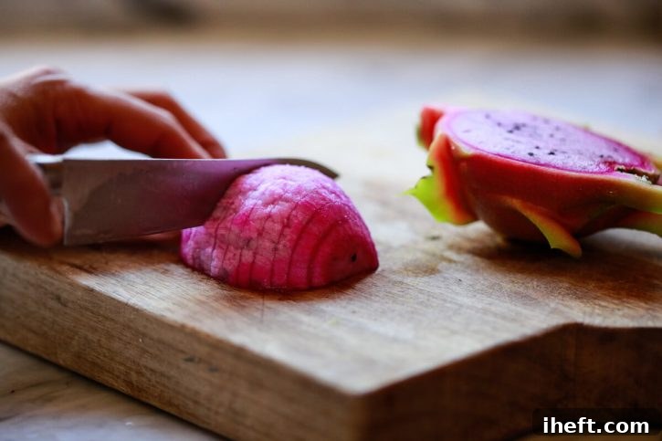A vibrant pink dragon fruit, perfectly peeled, is shown being sliced into elegant rounds on a rustic wooden cutting board, ready for serving.