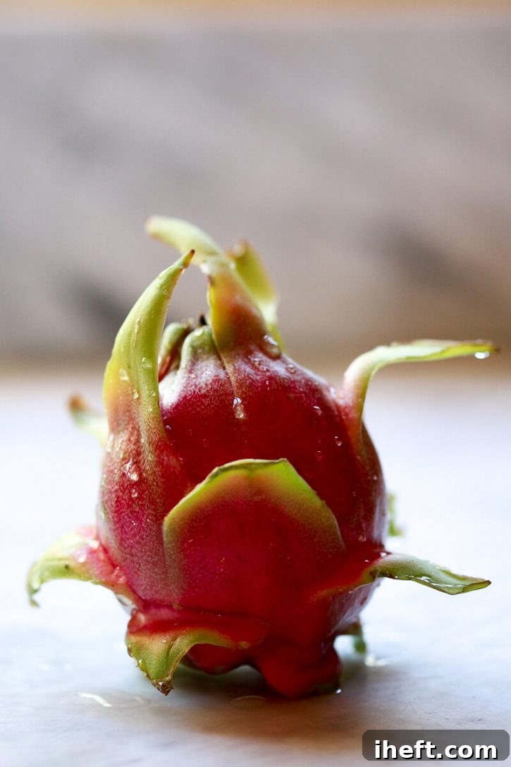 A whole red pitaya fruit sits on a white kitchen counter, ready to be cut.