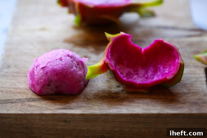 The vibrant pink skin is expertly peeled off of a dragon fruit half, revealing the smooth, edible flesh beneath.