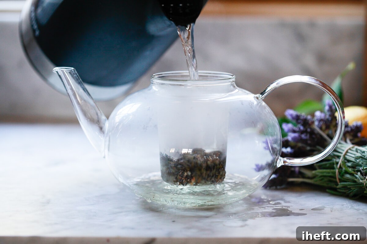 Boiling water is poured over dried lavender in a glass teapot infuser, beginning the steeping process.