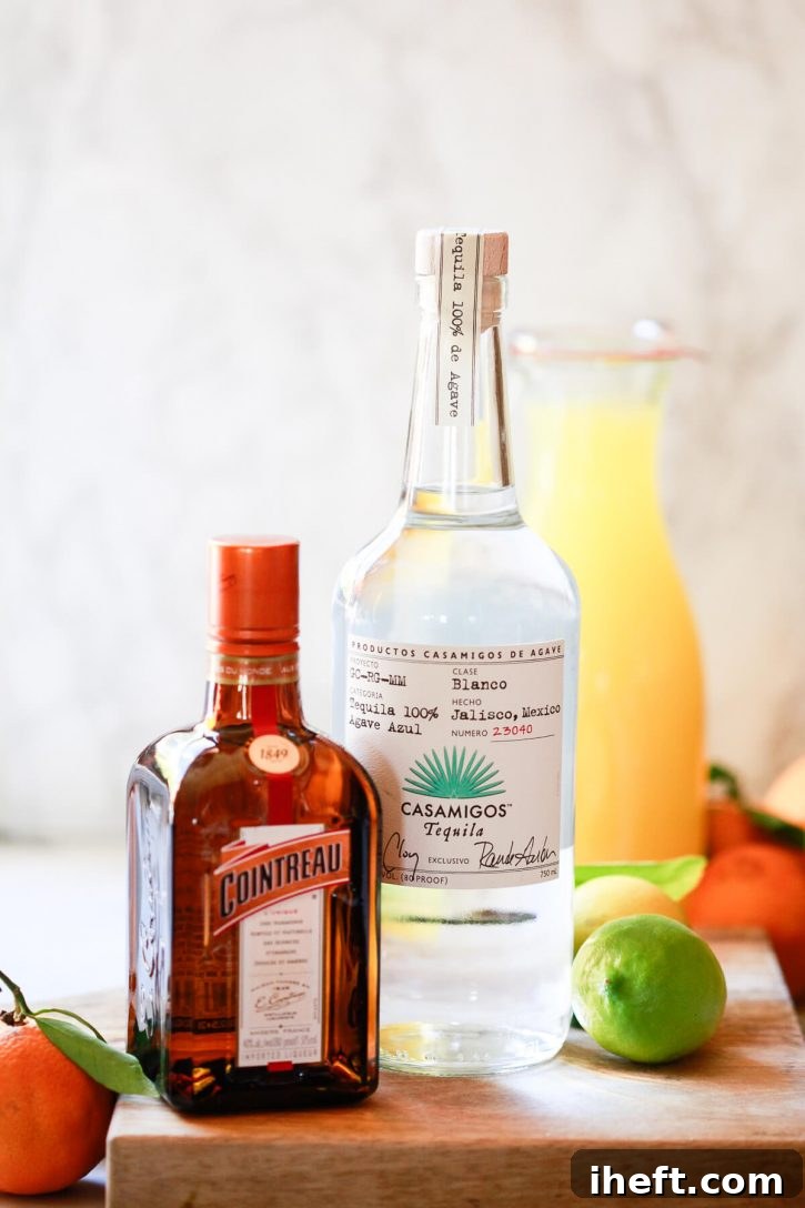A bottle of Casamigos tequila and a bottle of Cointreau, both premium spirits, elegantly stand on a kitchen counter, surrounded by a vibrant display of freshly picked citrus fruits. 