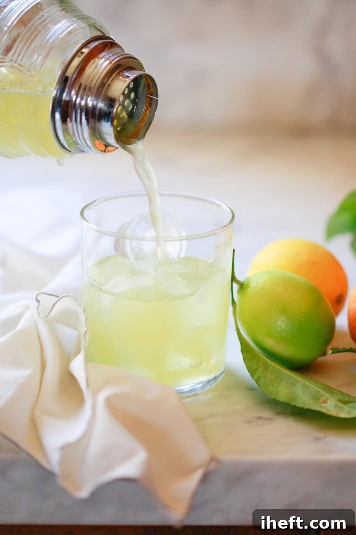 A skilled hand expertly pours a freshly shaken margarita from a sleek cocktail shaker into a salt-rimmed glass filled with ice. 