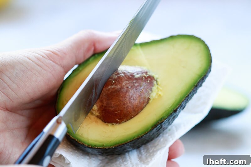 A knife hits the pit of an avocado half.