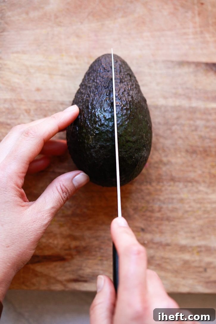 A photo of hands cutting a Haas avocado in half lengthwise with a knife. 