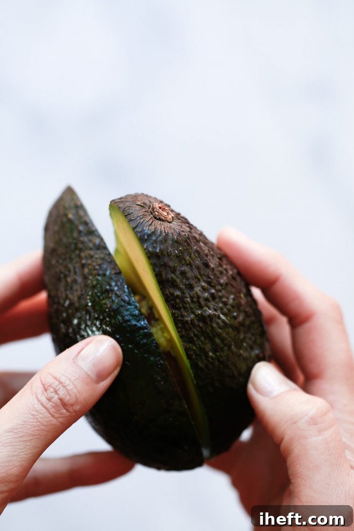 Close-up photography of hands twisting avocado halves apart. 