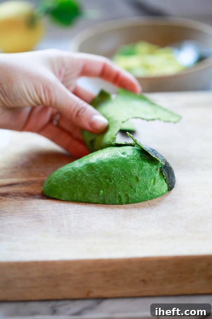 Photography of a hand peeling the skin away from half an avocado. 