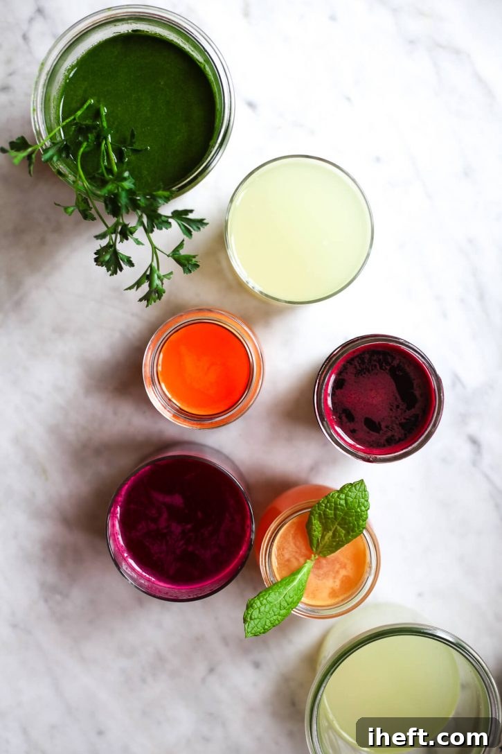 An overhead photo of colorful fresh juices in glasses on a white kitchen counter. These look like healthy juicing recipes. 