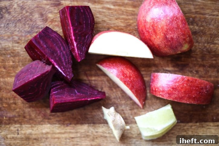 A raw beet, apple, ginger, and lemon on a cutting board for juicing. 