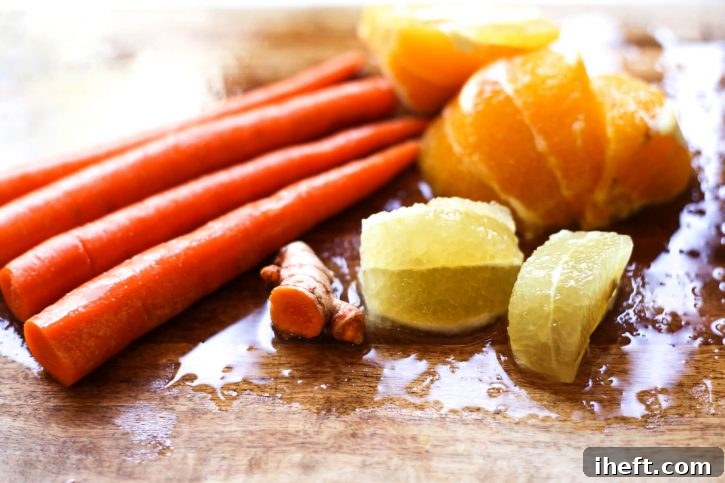 Carrots, turmeric, lemon, and orange prepared on a cutting board for juicing. 