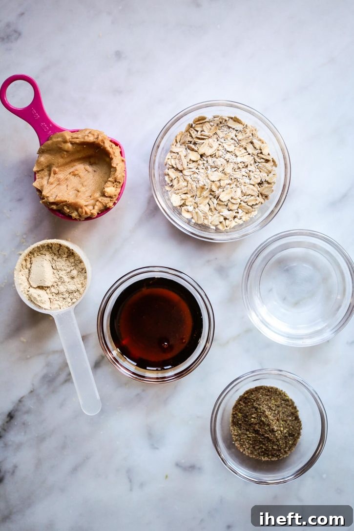 Five primary ingredients for making healthy peanut butter protein balls displayed neatly on a white marble countertop: a bowl of rolled oats, a jar of creamy peanut butter, a scoop of vanilla protein powder, a bottle of pure maple syrup, and a small dish of ground flaxseed meal. A glass of water is also present, highlighting the simple, wholesome components needed.
