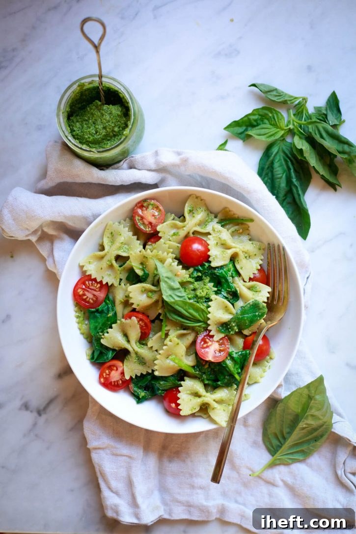 A bowl of farfalle pasta tossed with vibrant green vegan pesto, garnished with halved cherry tomatoes and fresh basil leaves, showcasing a simple yet elegant plant-based meal.