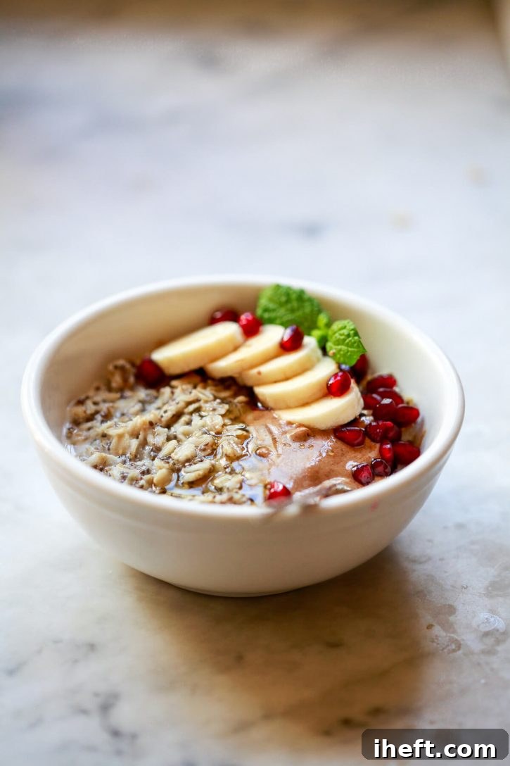 A vibrant close-up photograph of a white bowl overflowing with high-protein chia seed oatmeal, elegantly garnished with perfectly sliced banana, jewel-toned pomegranate seeds, and a luscious swirl of almond butter.
