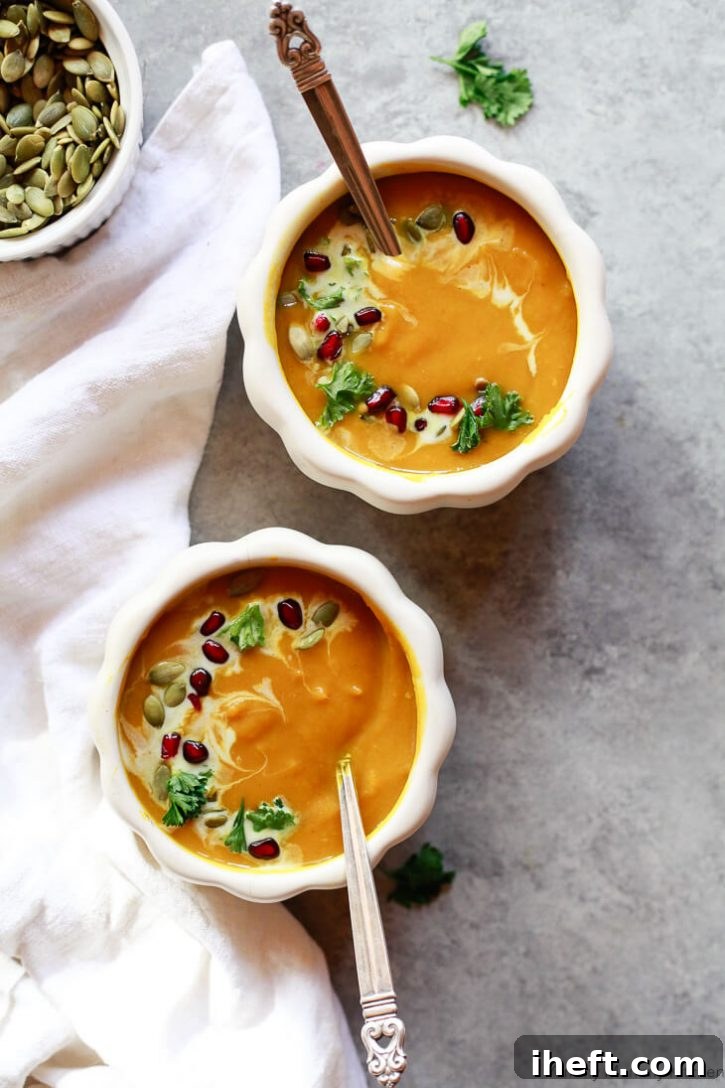Two elegantly presented bowls of creamy pumpkin butternut squash soup, garnished with jewel-like pomegranate seeds and crunchy pepitas, evoking the essence of autumn.