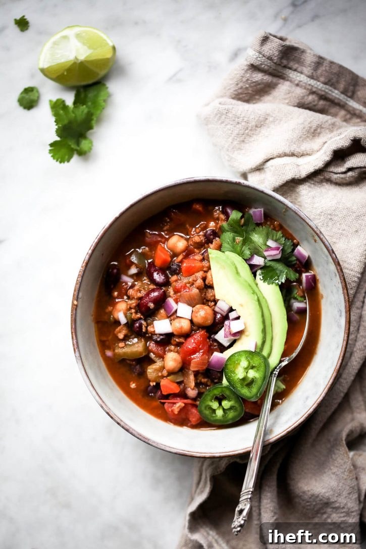 A generous bowl of vegan chili with chickpeas, elegantly topped with creamy avocado slices and fiery jalapeño rounds for a burst of flavor.