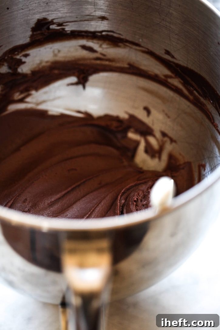 A glistening silver mixing bowl brimming with homemade vegan chocolate frosting, showcasing its smooth and rich texture. 