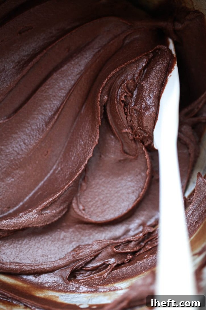 A captivating close-up photo reveals the rich, dark, and glossy texture of homemade dairy-free vegan chocolate frosting, ready for spreading. 
