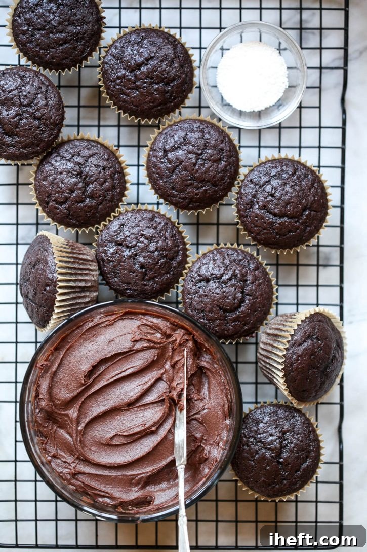Unfrosted vegan chocolate cupcakes on a cooling wrack next to a bowl of vegan chocolate frosting. 