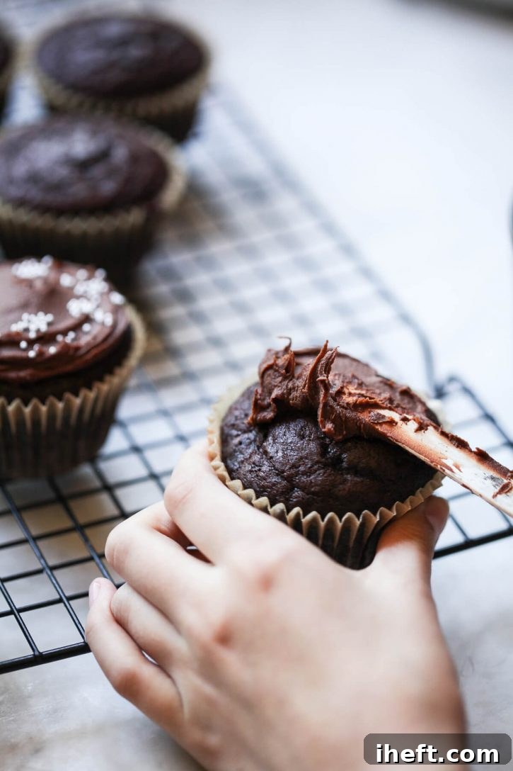 A photograph of child's hands spreading chocolate frosting onto a chocolate cupcake. 