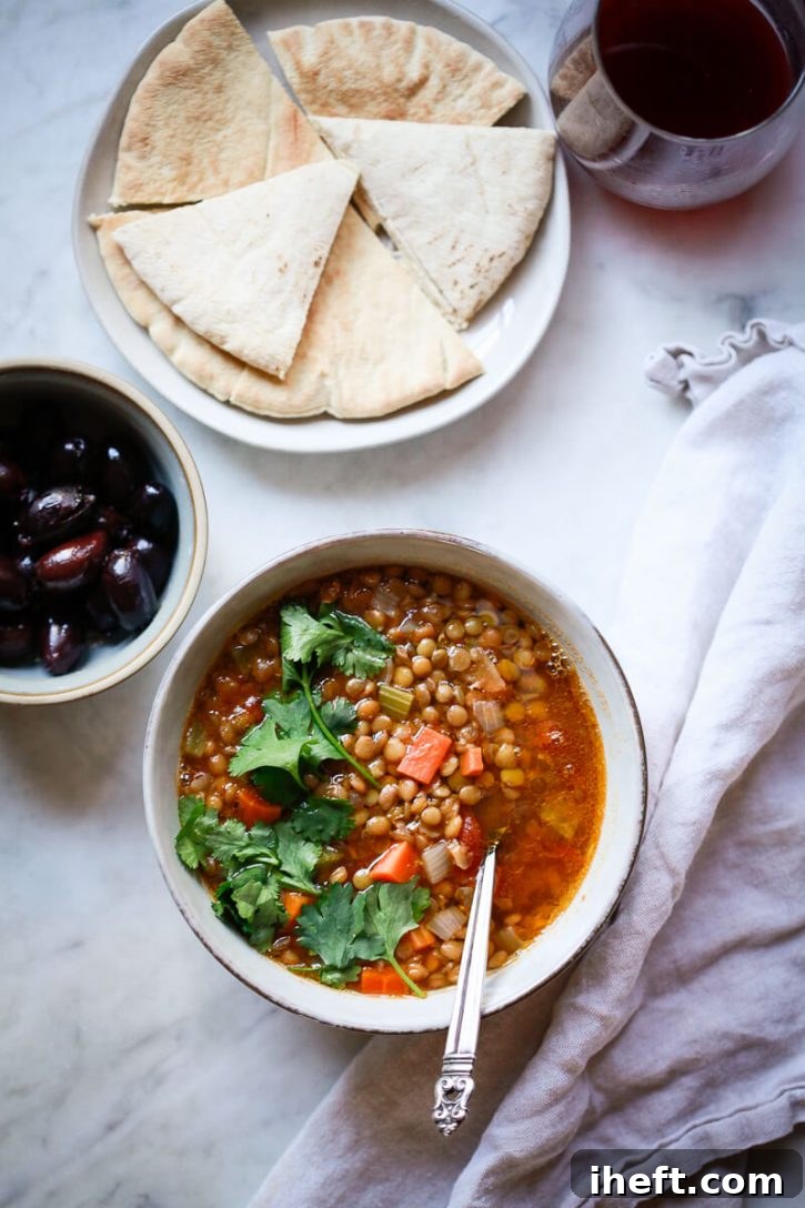 An overhead photo of Greek lentil soup, olives, pita bread, and wine. This is a healthy plant based dinner. 