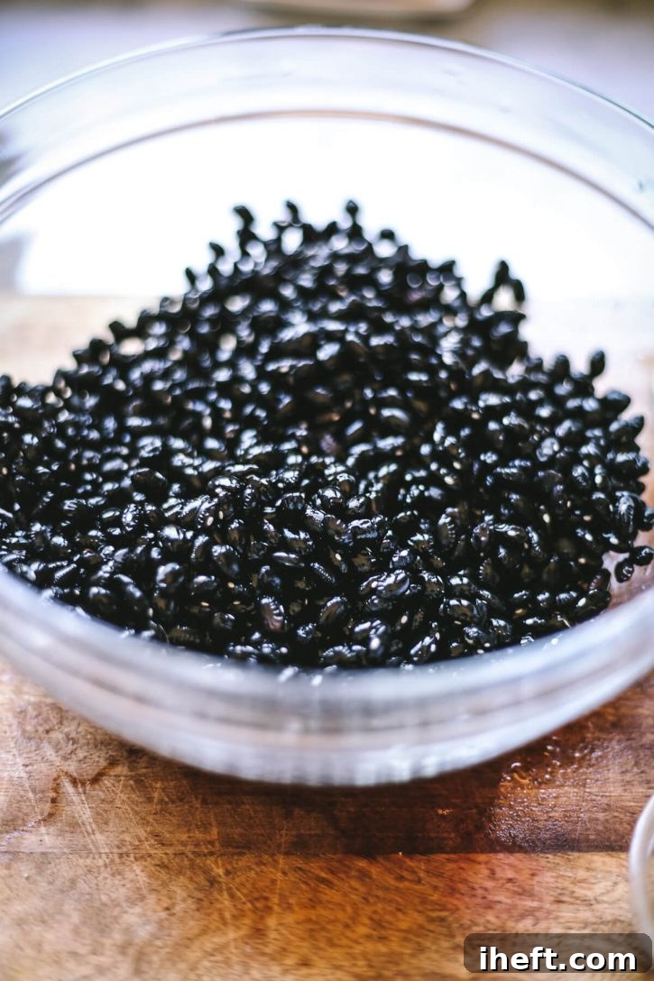 Dry black beans meticulously rinsed with water, showcased in a clear glass bowl, ready for cooking.
