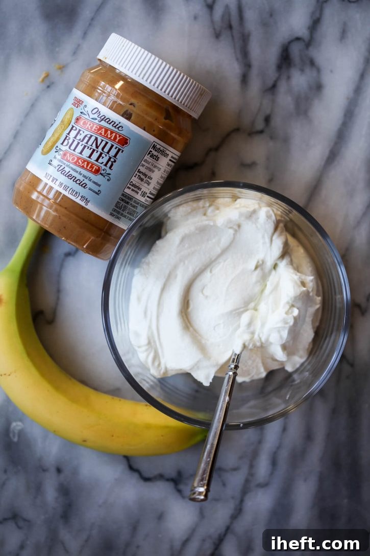 The simple, natural ingredients for homemade dog ice cream displayed on a sleek marble counter: creamy yogurt, rich peanut butter, and a ripe banana.