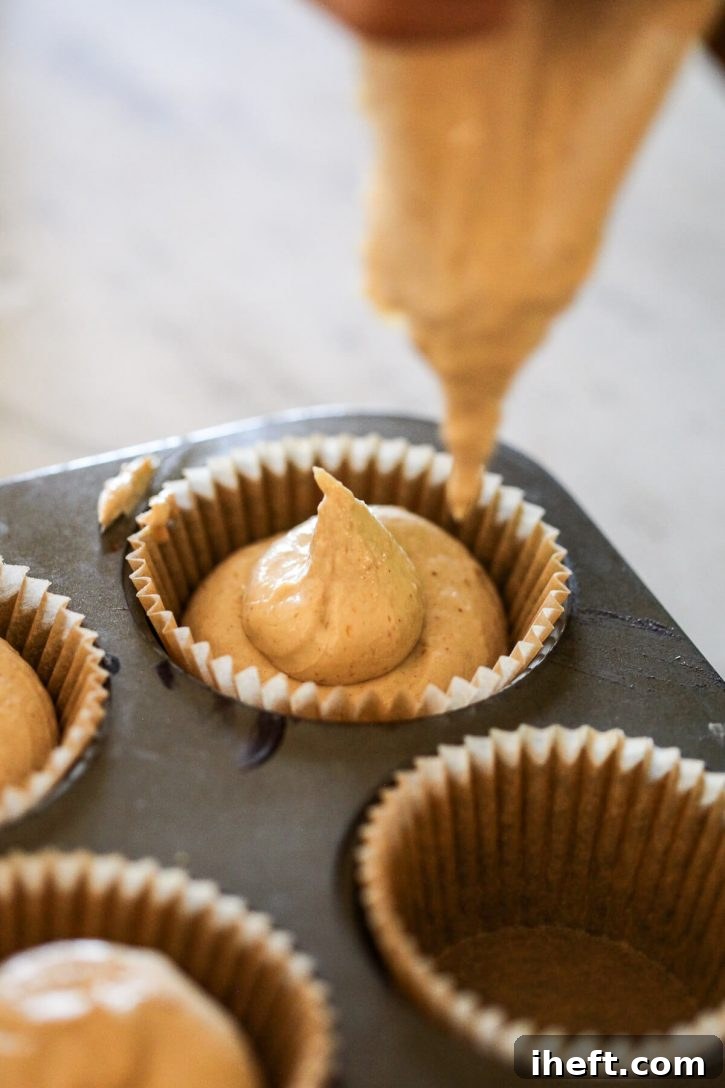 Smooth peanut butter dog ice cream mixture being piped neatly into the cups of a muffin tin, preparing for the freezing process.