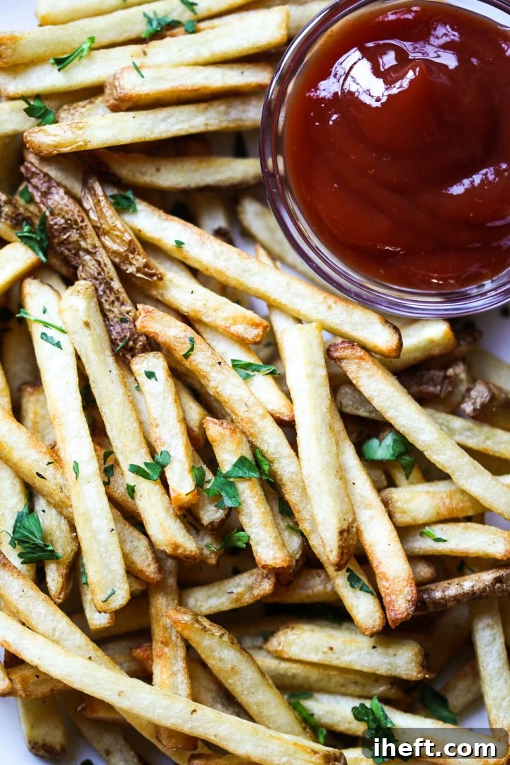 A close up photograph of perfectly cooked golden french fries garnished with parsley.