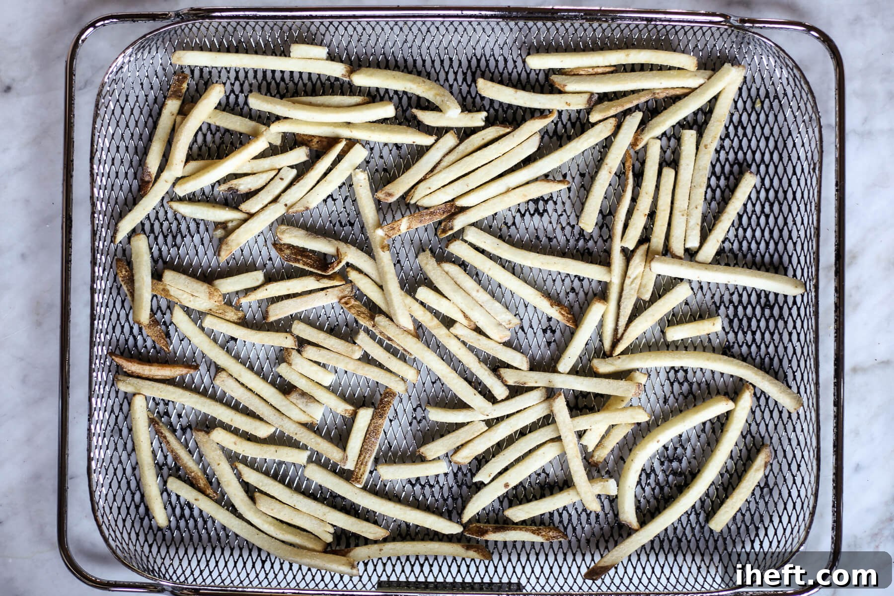 An overhead photograph of frozen French fries arranged in a air fryer basket.