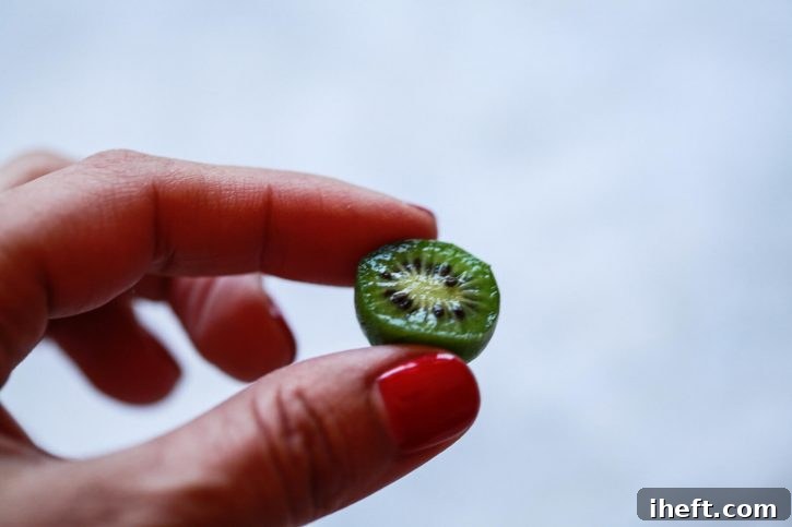 A tiny kiwi berry is held between two fingers. 