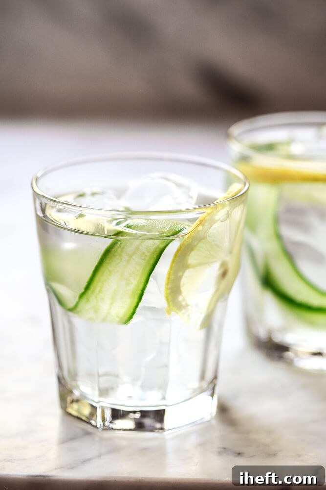 A close-up photo of two glasses filled with ice, water, lemon and cucumber ribbons. A beautiful and healthy cucumber water recipe for weight loss, detox, and clear skin. 