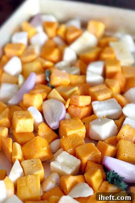 Butternut squash cubes and other vegetables roasting on a baking sheet, golden and tender.