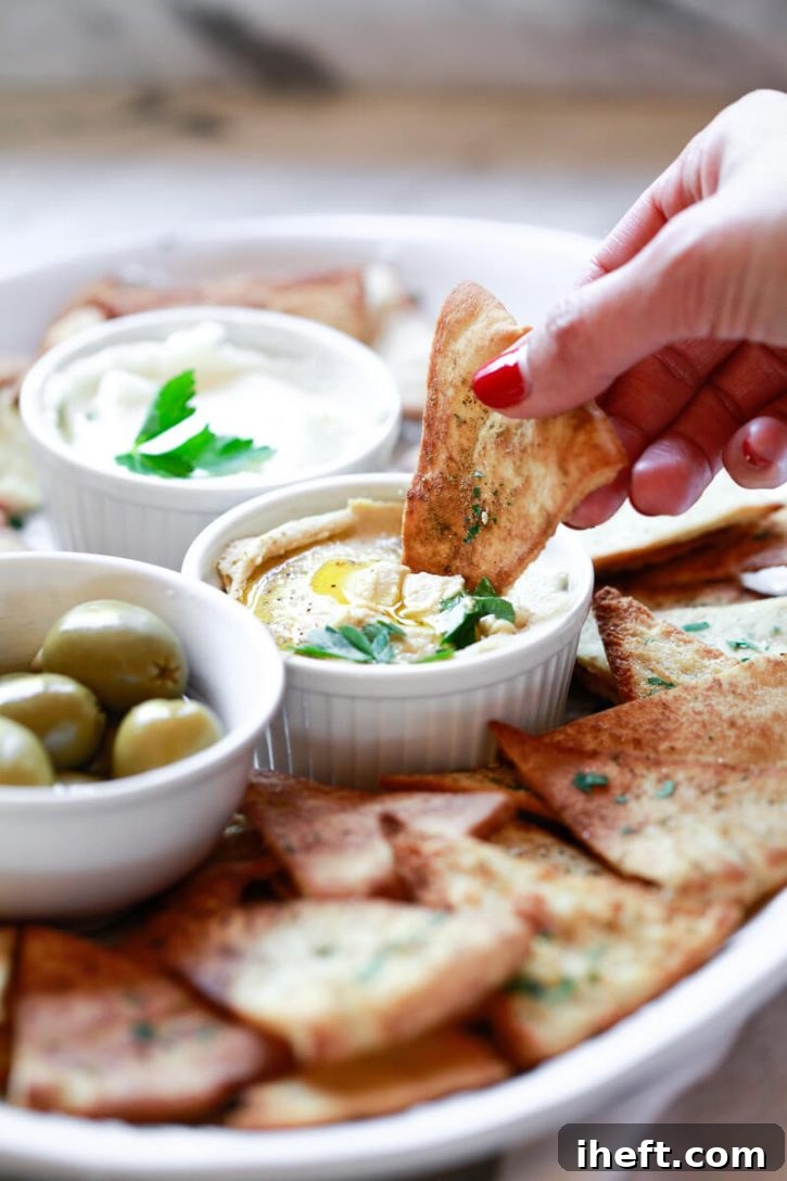 A homemade pita chip is dipped into a bowl of hummus.