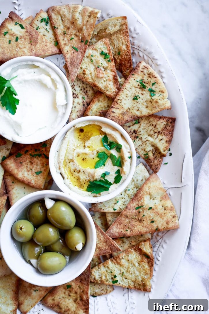 A white platter filled with homemade baked or air fried pita chips, hummus, labneh, and olives. An easy and healthy pita chip recipe.