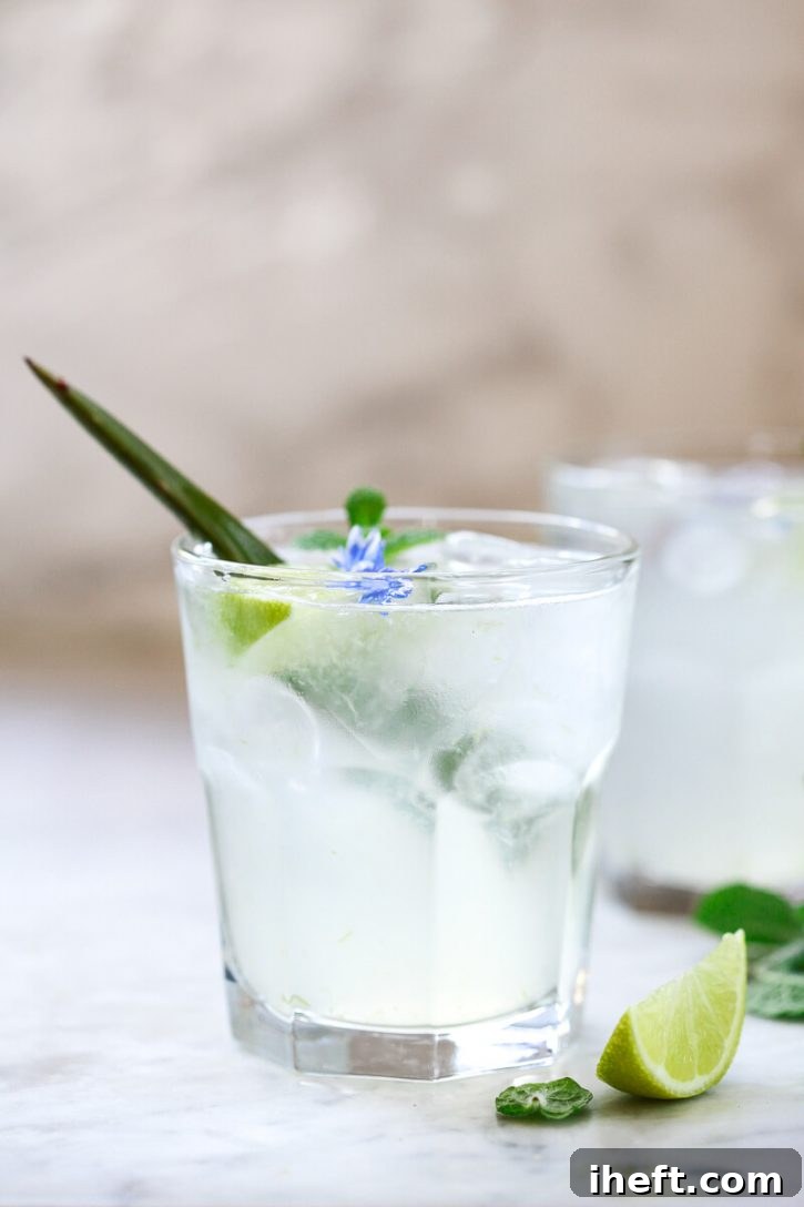 A beautifully clear glass filled with homemade aloe vera juice, garnished with a slice of lime, sits on a pristine white kitchen counter. This healthy, refreshing drink is celebrated for its benefits including clearer skin, natural detox, and support for weight management.