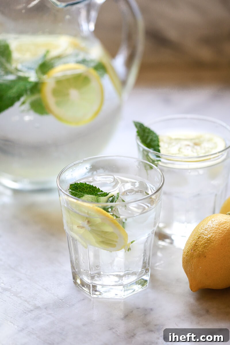 Glasses filled with lemon water garnished with mint on a white marble countertop.