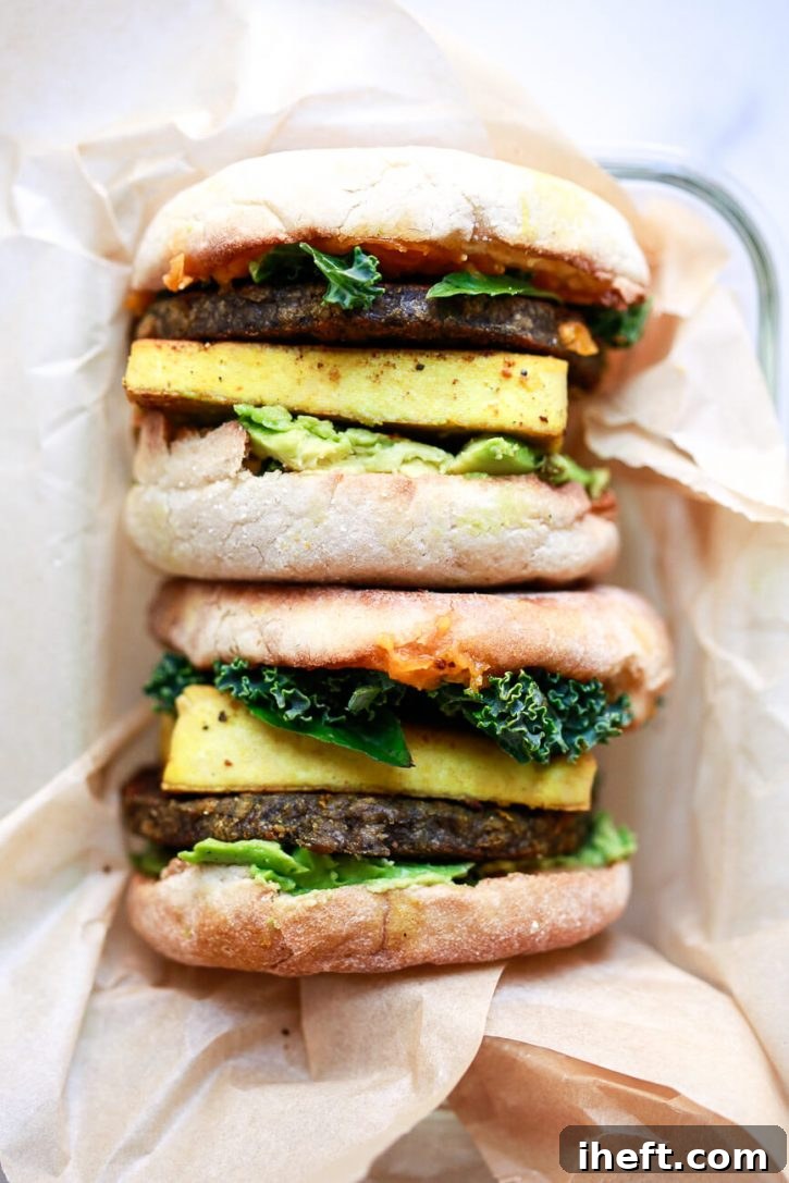 An overhead photo of two high protein vegan breakfast sandwiches made with vegan breakfast sausage, tofu, avocado, greens, and English Muffins. 