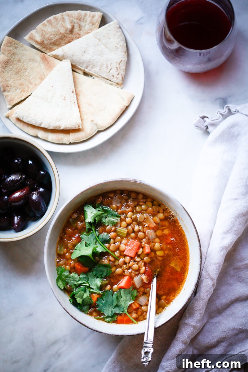 An overhead photo of Greek lentil soup next to olives, pita bread and wine. A great example of Mediterranean Diet recipes.