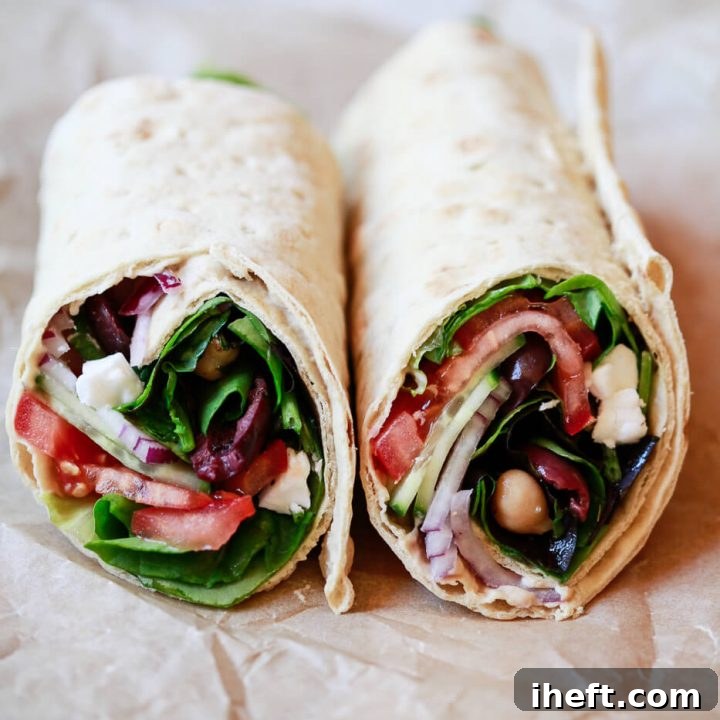 Mediterranean wraps cut in half filled with greens, tomato, feta, olives, cucumber, and onions.