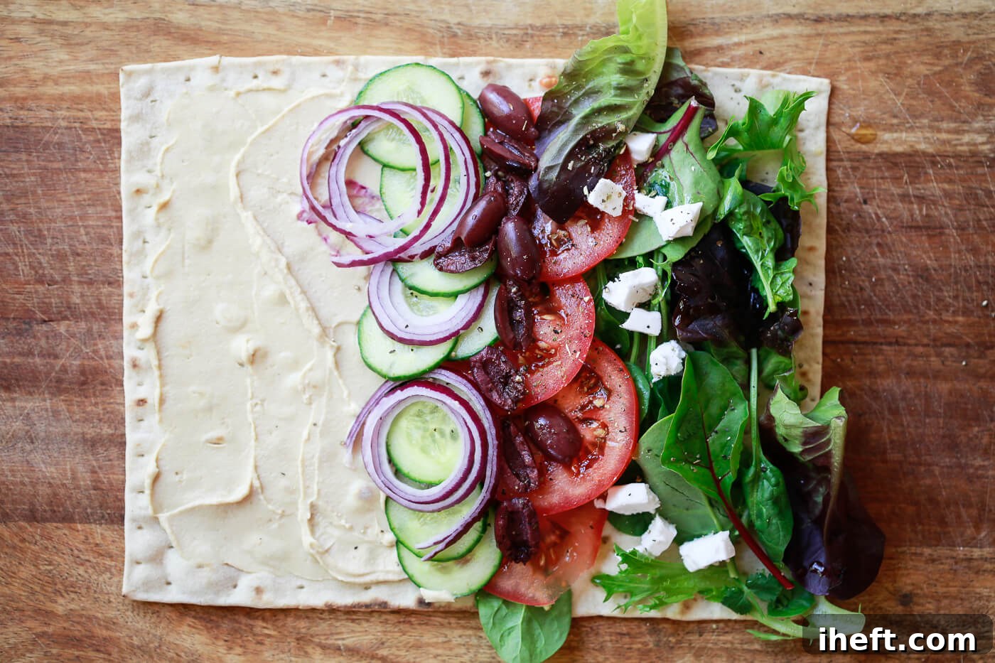 A piece of lavash flatbread is covered in hummus and vegetables.
