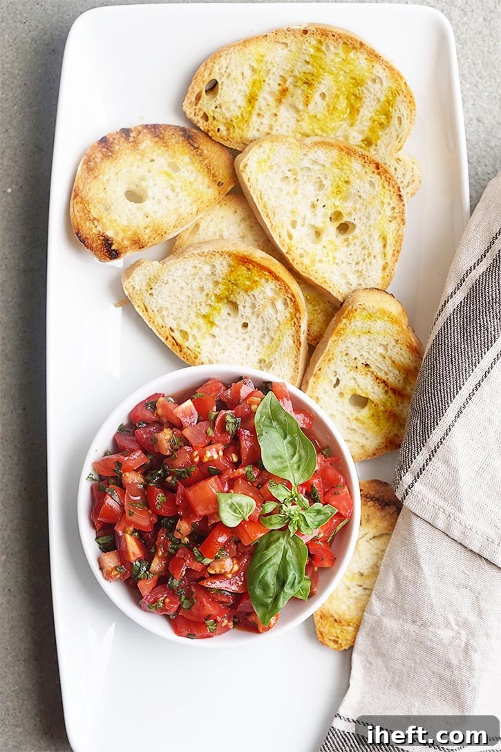 Overhead photo of a bowl of authentic Italian tomato bruschetta on a white platter with grilled Tuscan bread.