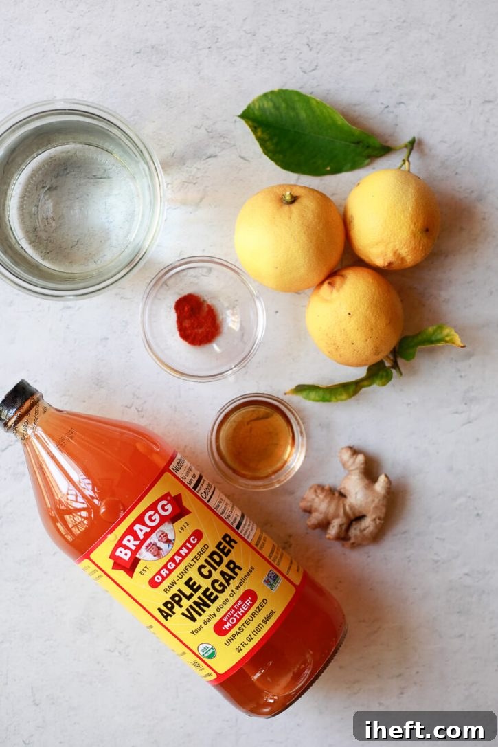 The ingredients for apple cider vinegar cleanse drinks on a kitchen counter: Bragg's apple cider vinegar, ginger, maple syrup, lemons, and cayenne. 